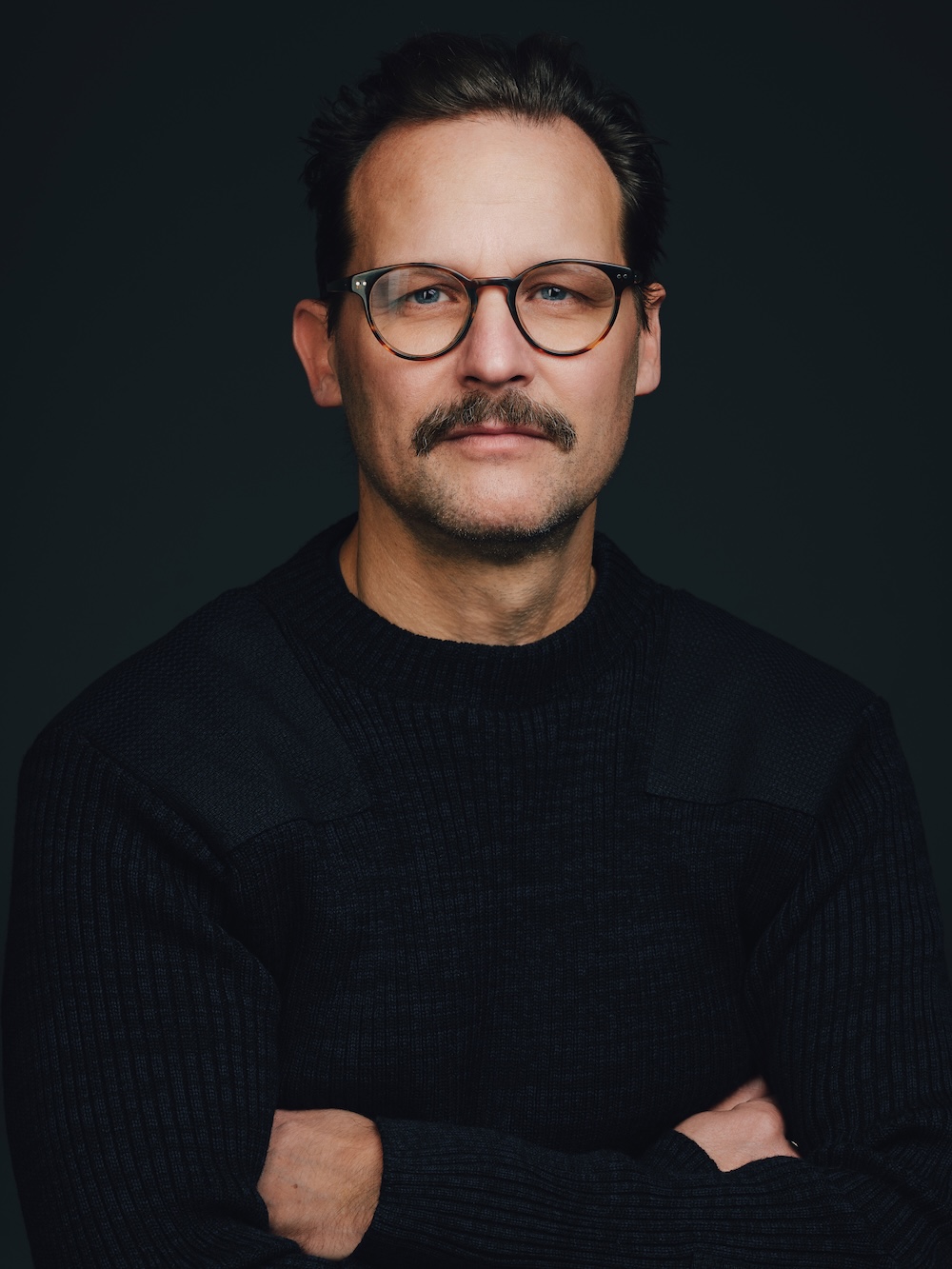 Stefan Vogel-Rosenberg looks into the camera with his arms crossed.